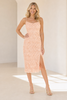 A woman modeling a light peach lace spaghetti-strap midi dress with a thigh-high slit, standing in a bright, minimalist cream-colored room.