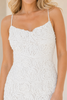 A close-up of a woman wearing a white textured lace spaghetti-strap dress against a soft beige background.